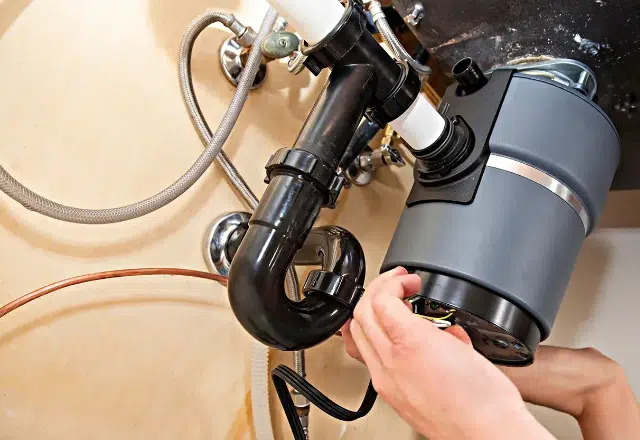 Plumber repairing a malfunctioning garbage disposal unit under a kitchen sink.