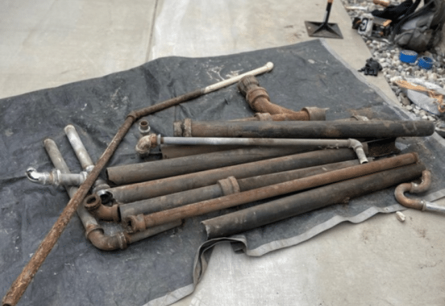 A collection of old, corroded pipes removed during a drain cleaning service, displayed on a tarp