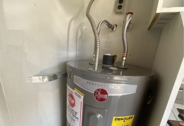 A Rheem water heater installed in a tight space with flexible connections, potential focus for emergency water heater repair.