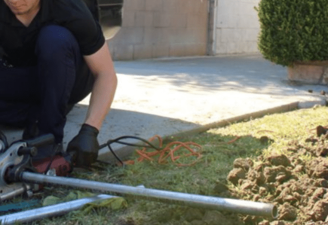 A technician working on pipes with a wrench near a gas line installation site, with tools and orange extension cords in the background.