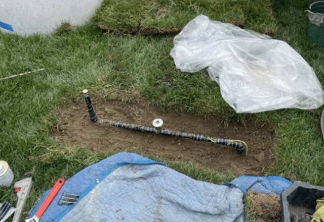 New gas line installation in progress with a section of black corrugated pipe exposed in a dugout trench in a grassy area.