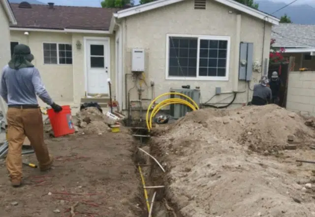 n outdoor scene of a residential gas line installation with workers, a large trench, and soil piled up around the yard.