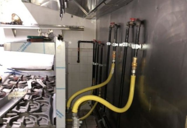 Commercial kitchen gas lines with yellow piping, showing a setup that may require inspection to repair a gas line leak.