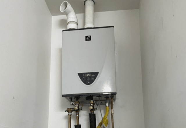 A single tankless electric water heater installed in a white closet, with pipes and a digital control panel visible