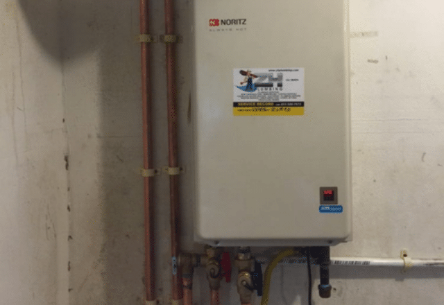 A Noritz tankless electric water heater installed next to copper pipes, representing a space-saving water heating solution.