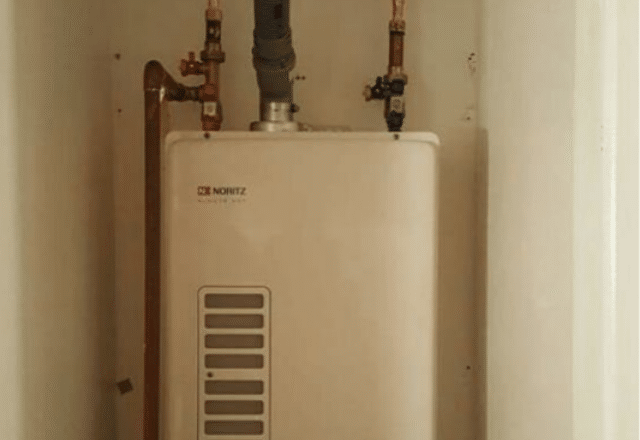 Compact tankless electric water heater fitted in a small space with accessible valves for easy maintenance.