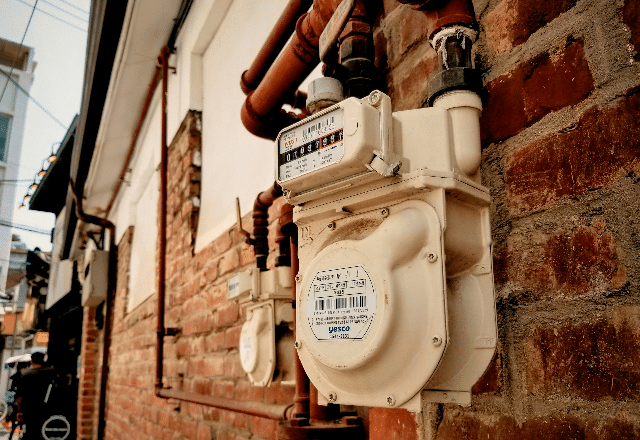 Outdoor gas meter and shut-off valves attached to a brick wall, part of the critical infrastructure maintained by gas plumbers