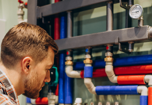 Gas plumber carefully inspecting a system of red and blue pipes with pressure gauges, reflecting the expertise required in the gas plumbing profession