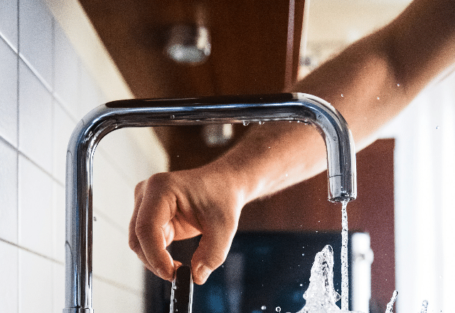 Water flowing from a chrome kitchen faucet with a person's hand testing the temperature, a common scene during the installation of a kitchen faucet.