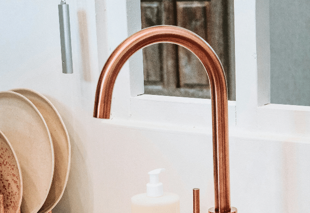 Elegant copper kitchen faucet against a white tiled backdrop with neutral-toned accessories, showcasing a stylish kitchen faucet installation