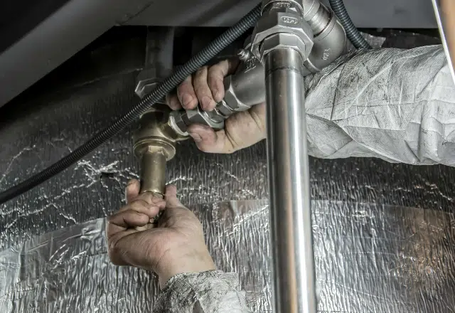 Hands of a plumber working on the pipes beneath a sink, an example of the detailed work provided by San Jose plumbing services