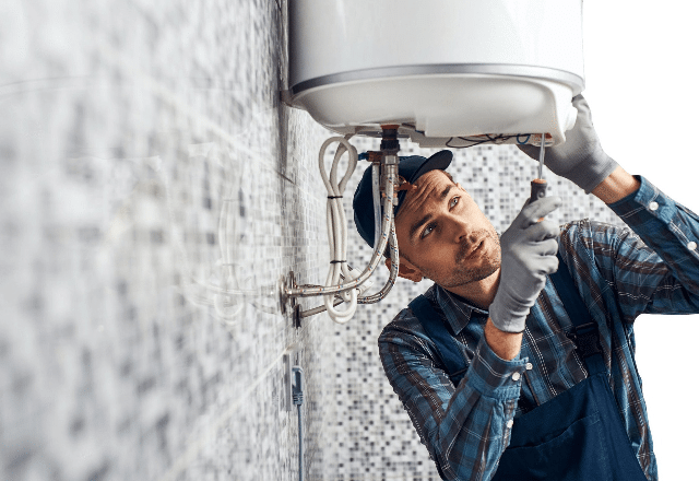Plumber in San Jose inspects the water connections under a wall-mounted water heater, showcasing typical plumbing maintenance work