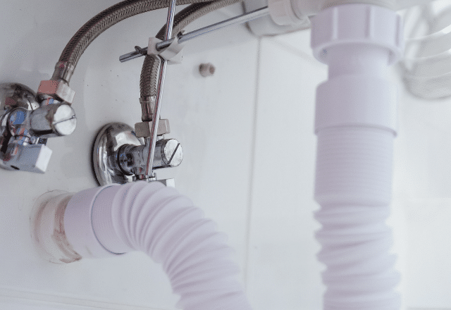 Under-sink view of white flexible drain pipe connections, demonstrating plumbing work commonly performed by Sacramento plumbers