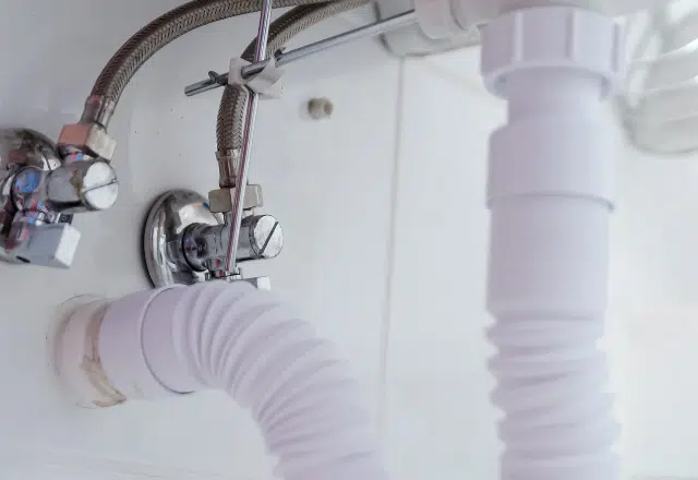 Under-sink view of white flexible drain pipe connections, demonstrating plumbing work commonly performed by Sacramento plumbers