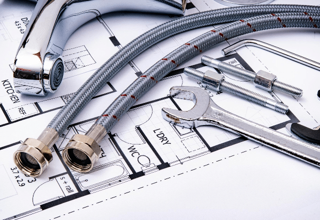Plumbing tools and materials, including flexible hoses and a wrench, laid out on architectural plans for a plumbing project in Sacramento