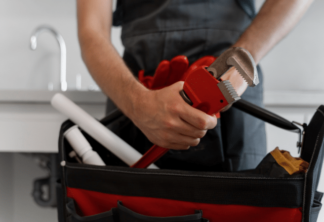 Plumber preparing tools for washing machine drain plumbing maintenance, with a red pipe wrench and PVC pipes suggesting repair or installation work