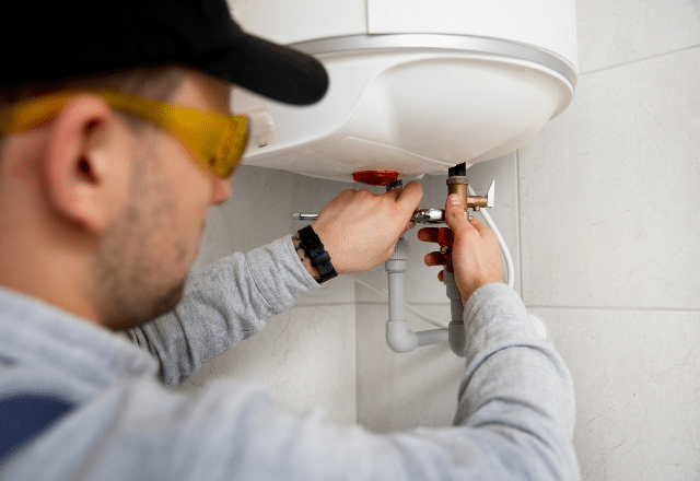 A skilled plumber in San Jose is fixing a water heater, focusing on the temperature control unit, which is a part of regular plumbing services