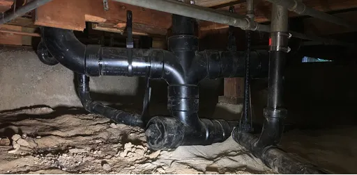 Black ABS drain and vent plumbing pipes installed in a home crawlspace or basement.