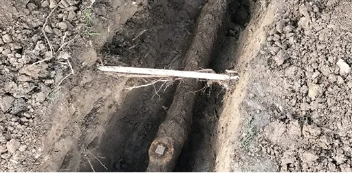 Underground main sewer line pipe exposed in a dirt trench for repair or replacement.
