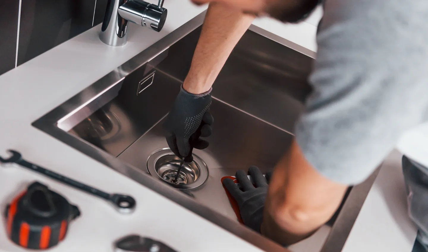 Plumber wearing gloves manually clearing a clogged kitchen sink drain