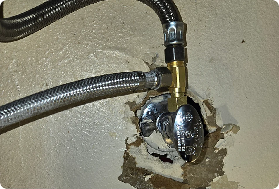 Chrome angle stop shutoff valve with braided supply lines coming out of a damaged wall