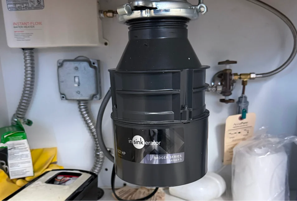 Garbage disposal unit mounted under a kitchen sink next to an electrical outlet